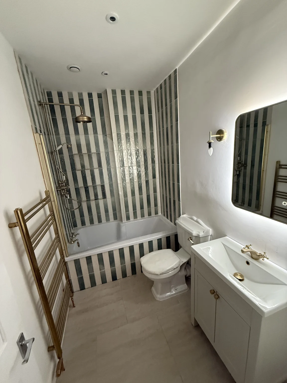 Bathroom with green-and-cream vertical tiles, a bath and a vanity unit.
