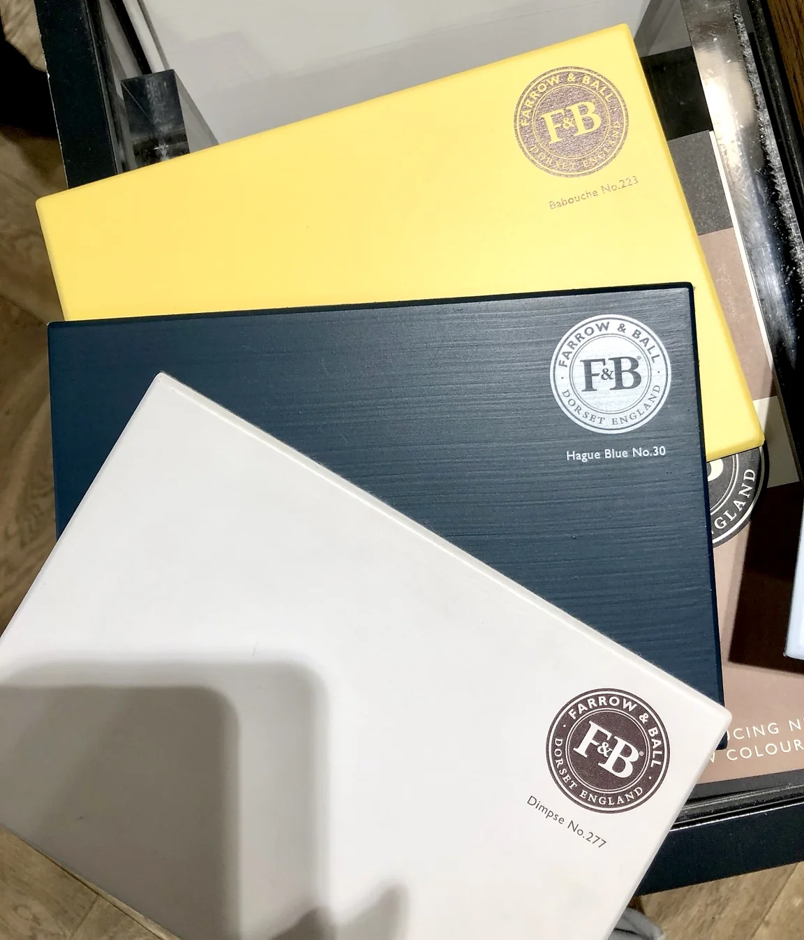 Three Farrow & Ball sample boards fanned out: Babouche No.223 yellow, Hague Blue No.30 and Dimpse No.277 off-white.