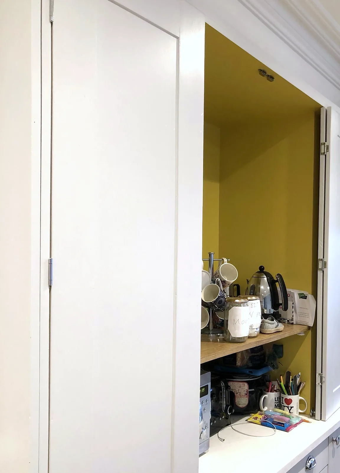 Bi-fold cupboard doors opened to show a yellow-lined cupboard with an oak shelf above the worktop.